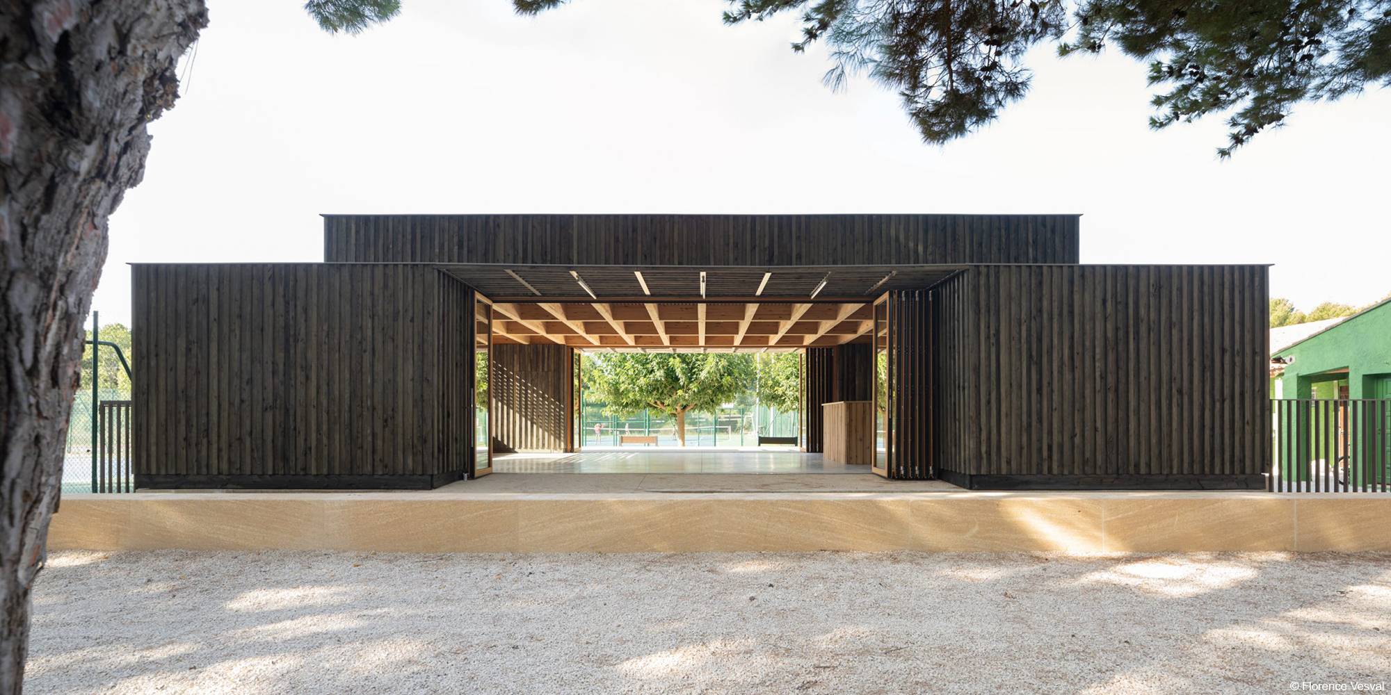 Salle polyvalente en bois lamellé collé sur socle en pierre avec bardage en bois brulé